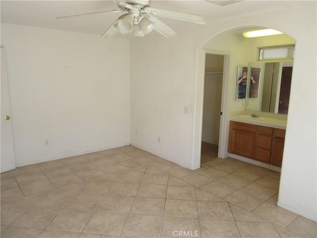 unfurnished bedroom featuring a spacious closet, a closet, light tile patterned floors, arched walkways, and a sink