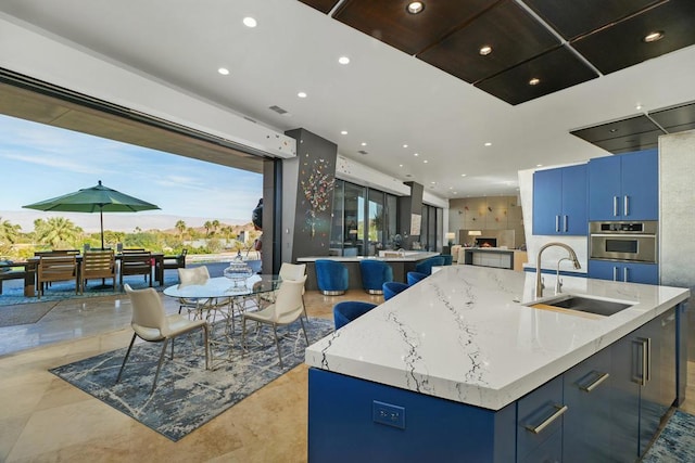 kitchen featuring blue cabinets, stainless steel oven, a kitchen island with sink, and sink