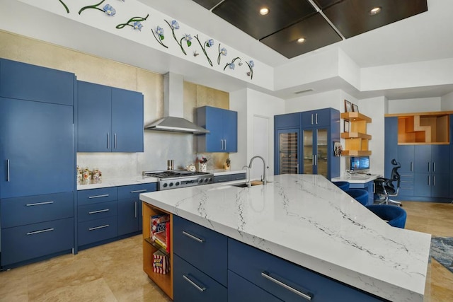 kitchen featuring sink, a high ceiling, a kitchen island with sink, blue cabinetry, and wall chimney exhaust hood