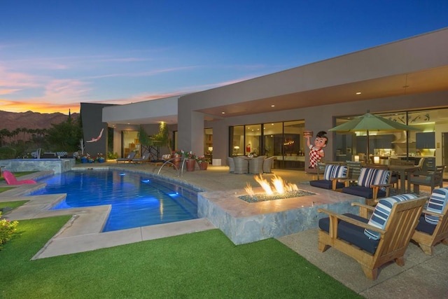 pool at dusk featuring pool water feature, an outdoor fire pit, a mountain view, and a patio area