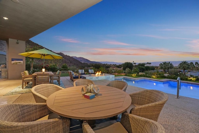 pool at dusk featuring a mountain view, a fire pit, and a patio