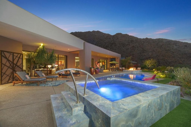 pool at dusk with a mountain view, a patio, and an in ground hot tub