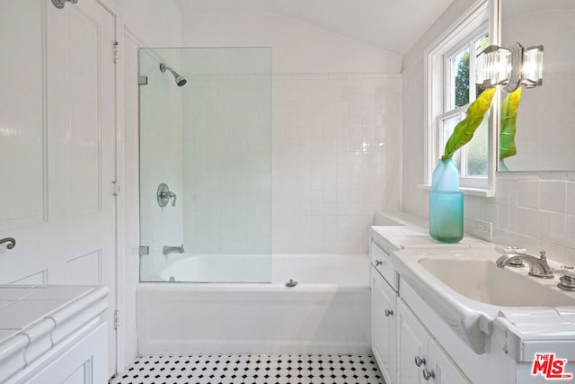 bathroom with tiled shower / bath combo, vaulted ceiling, tasteful backsplash, and vanity