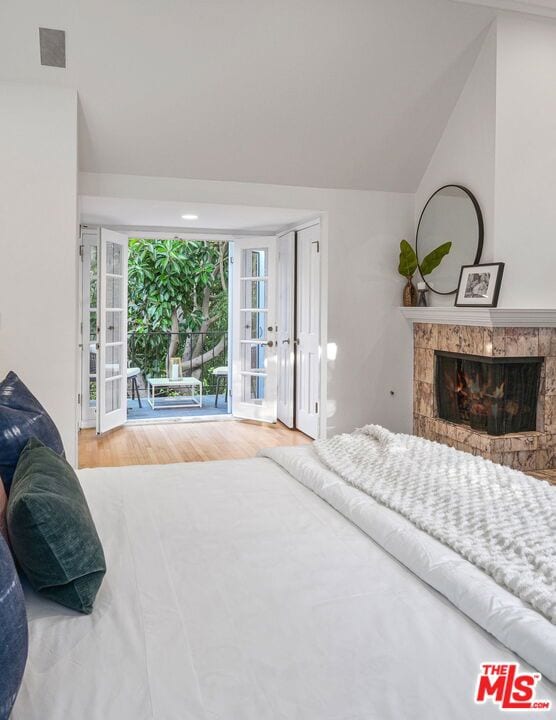 bedroom with hardwood / wood-style flooring, vaulted ceiling, a stone fireplace, access to outside, and french doors