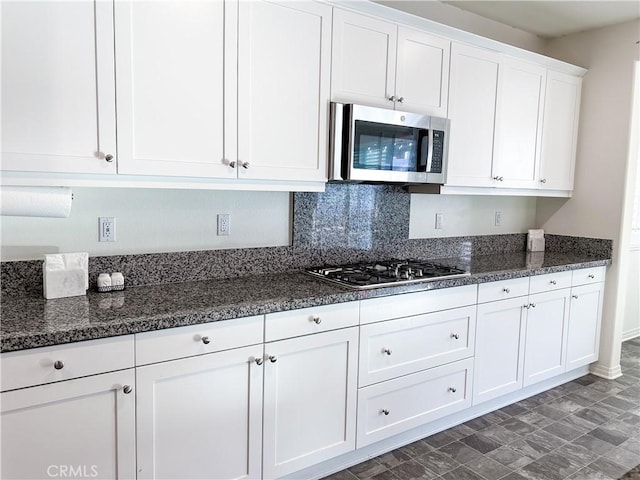 kitchen featuring white cabinetry, stainless steel appliances, tasteful backsplash, and dark stone counters