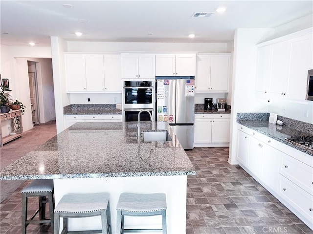 kitchen featuring a breakfast bar area, a center island with sink, dark stone countertops, appliances with stainless steel finishes, and white cabinets