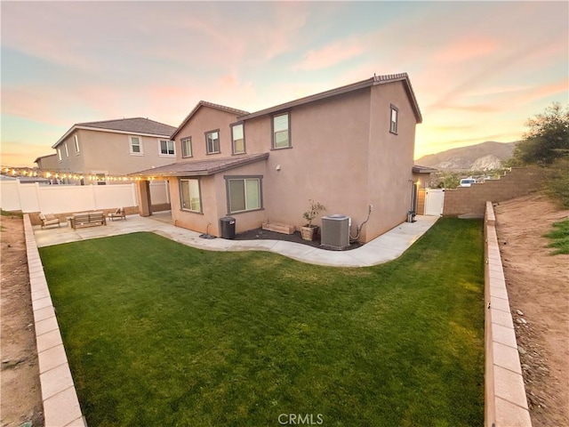 back house at dusk with cooling unit, a mountain view, a patio area, and a lawn