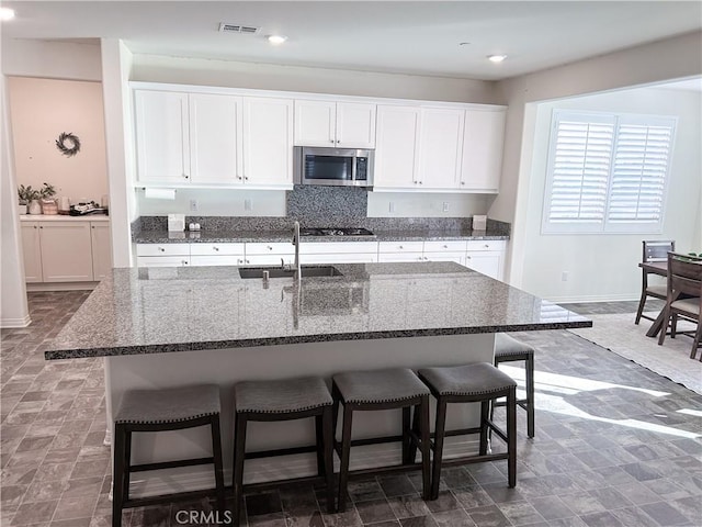 kitchen featuring sink, white cabinetry, a kitchen breakfast bar, an island with sink, and black gas stovetop