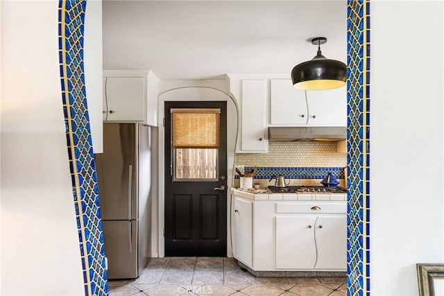 kitchen featuring light tile patterned flooring, stainless steel refrigerator, tile counters, white cabinets, and backsplash