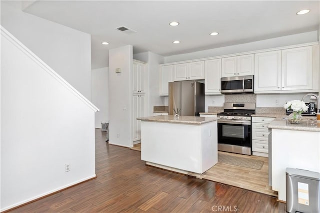 kitchen featuring a kitchen island, white cabinetry, stainless steel appliances, light stone countertops, and dark wood-type flooring