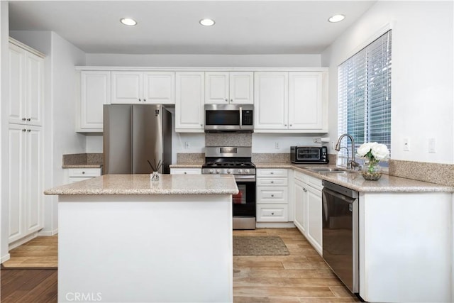 kitchen with white cabinetry, appliances with stainless steel finishes, a kitchen island, and light wood-type flooring