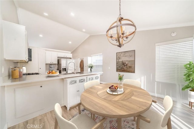 dining room featuring an inviting chandelier, lofted ceiling, sink, and light hardwood / wood-style floors