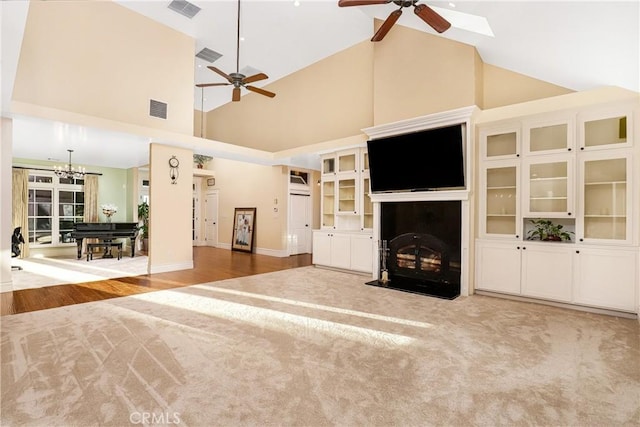 unfurnished living room featuring ceiling fan with notable chandelier and high vaulted ceiling