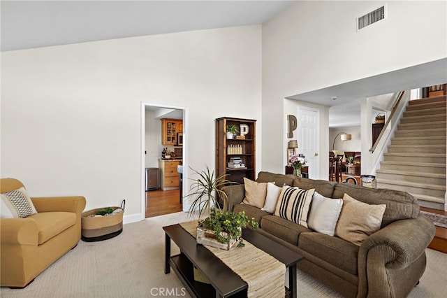 living area with high vaulted ceiling, light colored carpet, visible vents, baseboards, and stairs