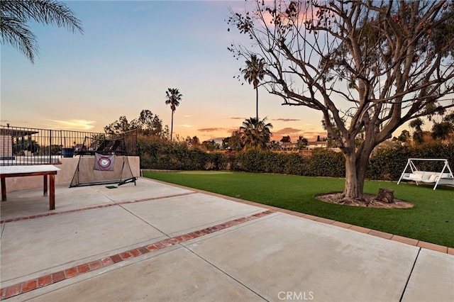 patio terrace at dusk featuring a lawn and fence