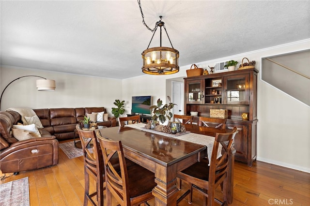 dining room featuring a textured ceiling, a chandelier, wood finished floors, and ornamental molding