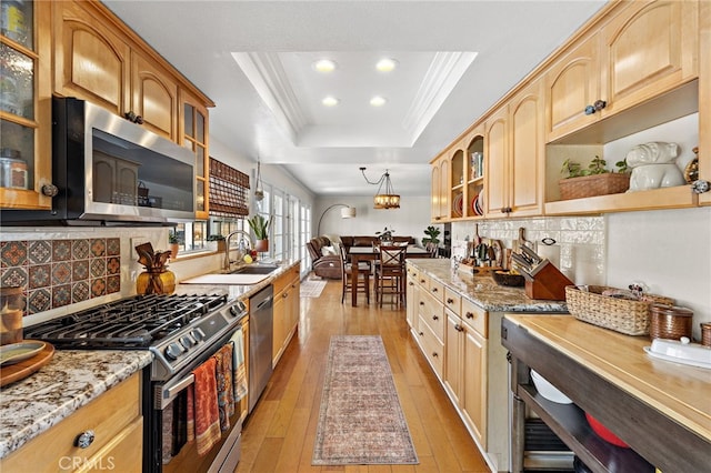 kitchen with a raised ceiling, glass insert cabinets, appliances with stainless steel finishes, light stone countertops, and a sink