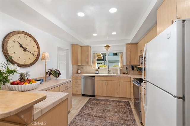 kitchen with sink, appliances with stainless steel finishes, backsplash, tile counters, and light brown cabinetry