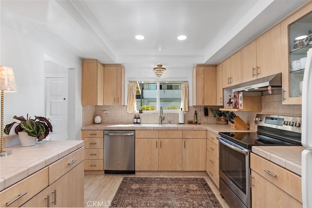 kitchen with appliances with stainless steel finishes, sink, light brown cabinets, and tile counters