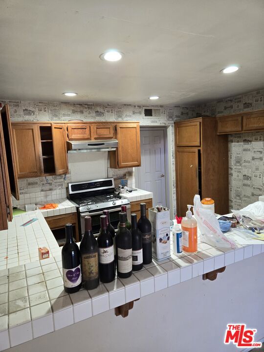 kitchen with gas range, a breakfast bar, tile countertops, and kitchen peninsula