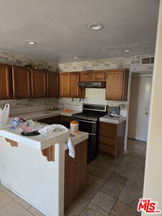 kitchen with range with two ovens, tile counters, a kitchen bar, and kitchen peninsula