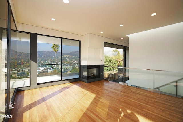 unfurnished living room featuring a multi sided fireplace, a mountain view, and wood-type flooring