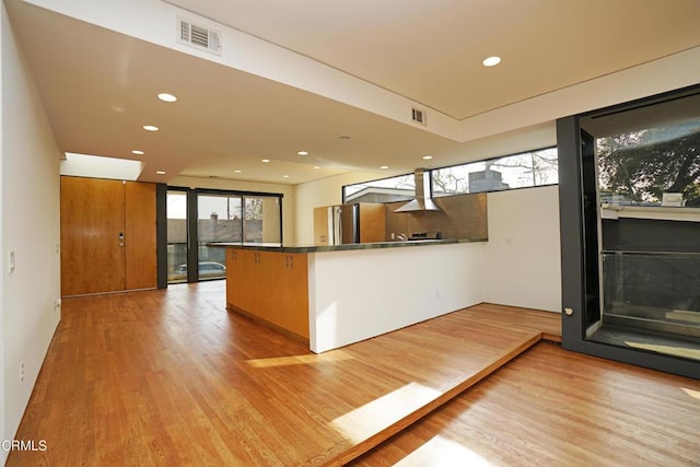 kitchen featuring stainless steel refrigerator, kitchen peninsula, light hardwood / wood-style flooring, and wall chimney range hood