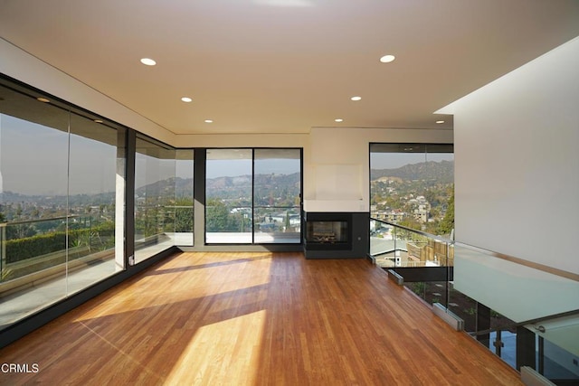 unfurnished living room with hardwood / wood-style flooring, floor to ceiling windows, a mountain view, and a multi sided fireplace