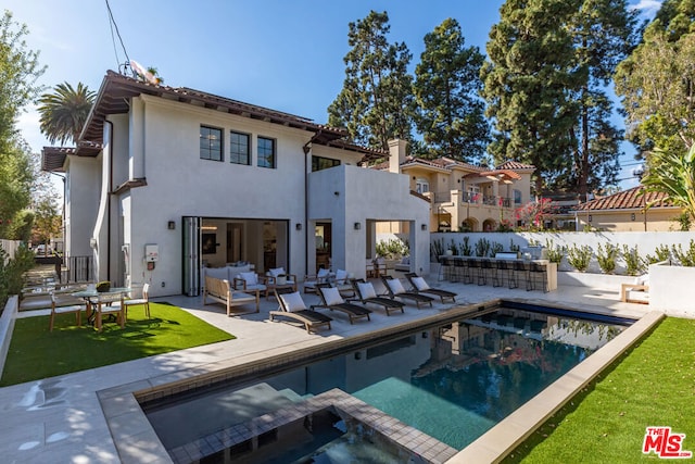 rear view of house featuring a fenced in pool, a yard, outdoor lounge area, a patio area, and a bar