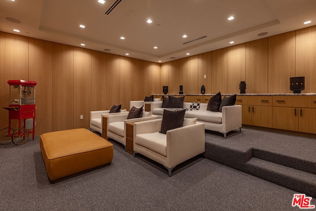 cinema featuring a tray ceiling, dark carpet, and wood walls