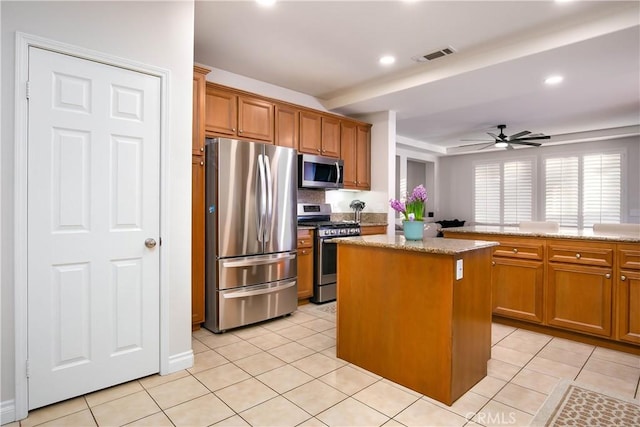 kitchen with light stone counters, light tile patterned floors, a center island, and appliances with stainless steel finishes