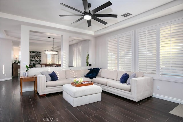 living room with dark wood-type flooring, ceiling fan, and a raised ceiling