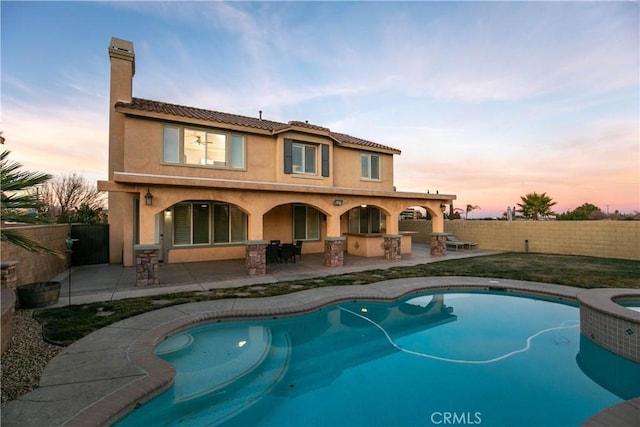 back house at dusk featuring a bar, a pool with hot tub, and a patio area