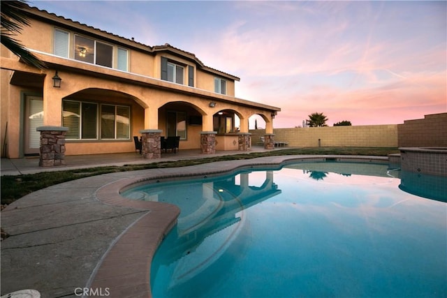 pool at dusk featuring a patio and an outdoor bar