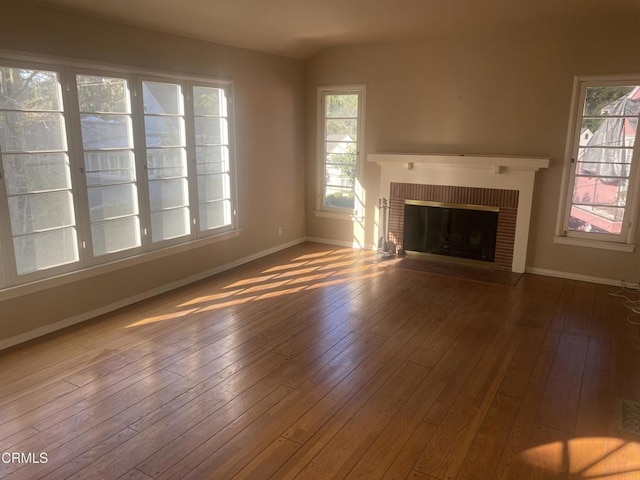 unfurnished living room with hardwood / wood-style flooring, a healthy amount of sunlight, and a brick fireplace