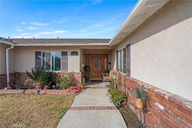 doorway to property with a yard, brick siding, and stucco siding