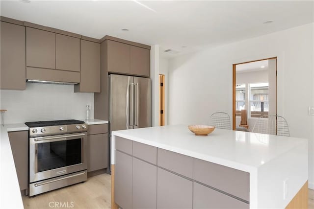 kitchen with appliances with stainless steel finishes, gray cabinetry, decorative backsplash, a center island, and light wood-type flooring