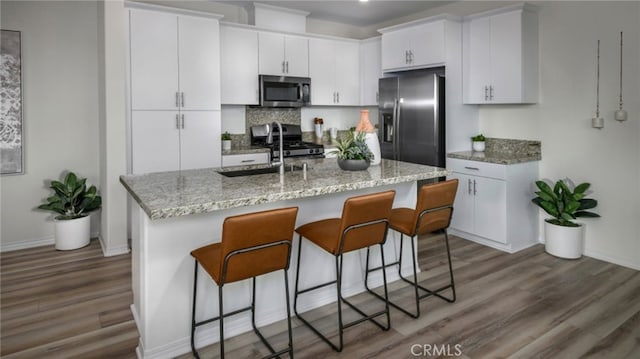 kitchen with appliances with stainless steel finishes, dark hardwood / wood-style flooring, an island with sink, and white cabinets