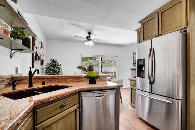 kitchen featuring appliances with stainless steel finishes, sink, ceiling fan, light hardwood / wood-style floors, and light stone countertops