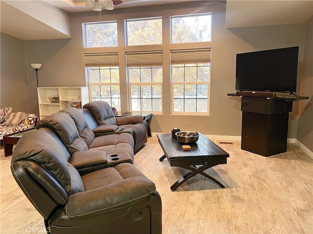 living room with ceiling fan, a towering ceiling, and light hardwood / wood-style floors