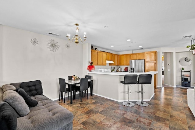 kitchen featuring a chandelier, hanging light fixtures, stainless steel fridge, a kitchen breakfast bar, and kitchen peninsula