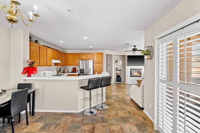 kitchen with a breakfast bar area, range, hanging light fixtures, stainless steel fridge, and kitchen peninsula