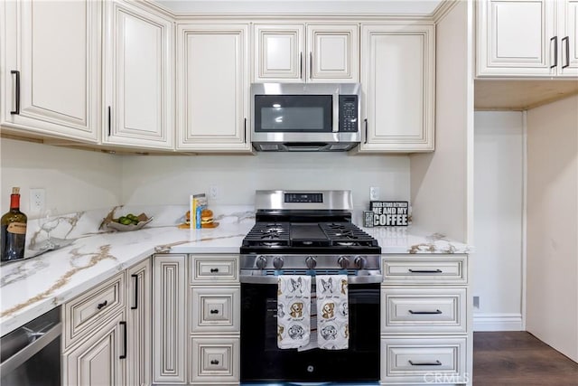 kitchen featuring appliances with stainless steel finishes, dark hardwood / wood-style flooring, light stone countertops, and cream cabinetry