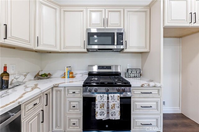 kitchen with light stone counters, dark wood-type flooring, cream cabinetry, and appliances with stainless steel finishes