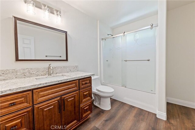 full bathroom featuring bath / shower combo with glass door, hardwood / wood-style floors, vanity, and toilet