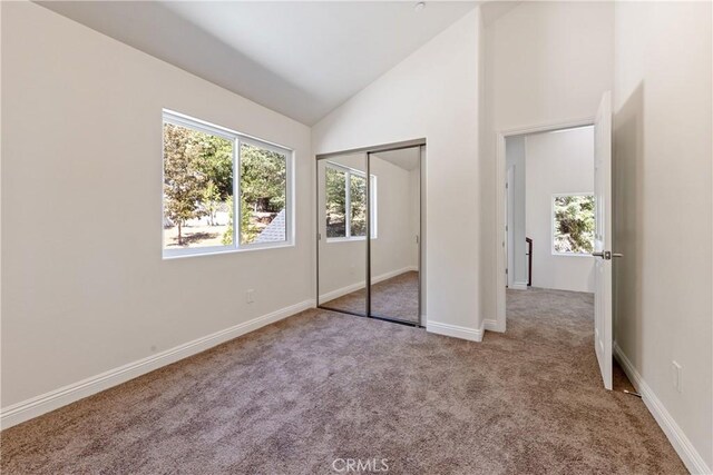 unfurnished bedroom with light colored carpet, high vaulted ceiling, and a closet