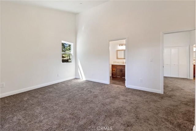 unfurnished bedroom with connected bathroom, dark colored carpet, and a high ceiling