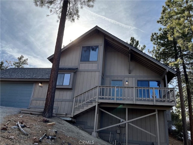 back of property featuring a deck, roof with shingles, stairway, and an attached garage