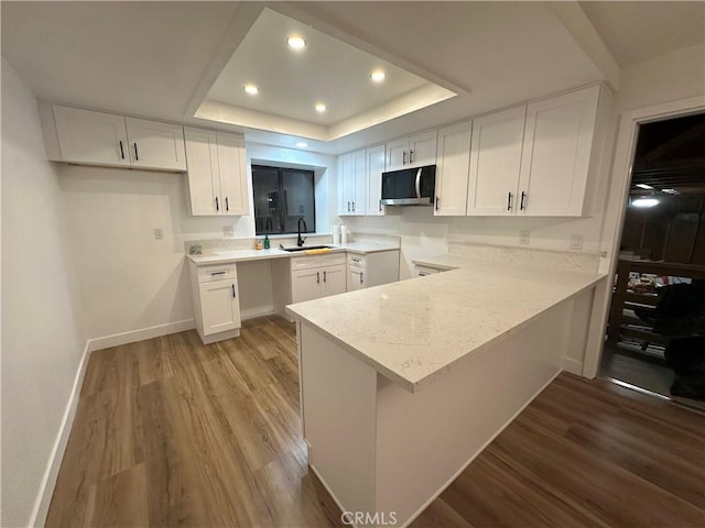 kitchen with sink, white cabinets, hardwood / wood-style flooring, kitchen peninsula, and a raised ceiling