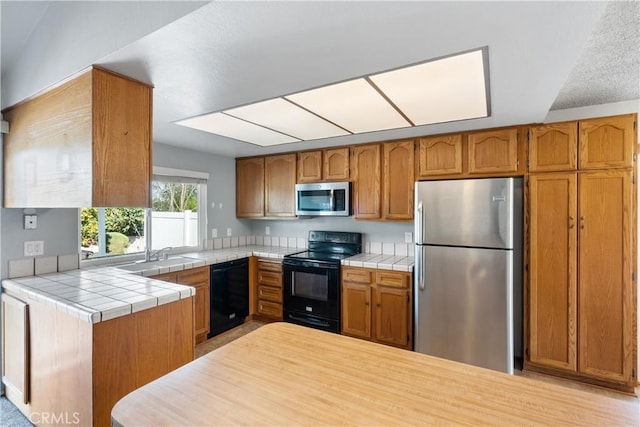 kitchen with sink, tile countertops, black appliances, and kitchen peninsula